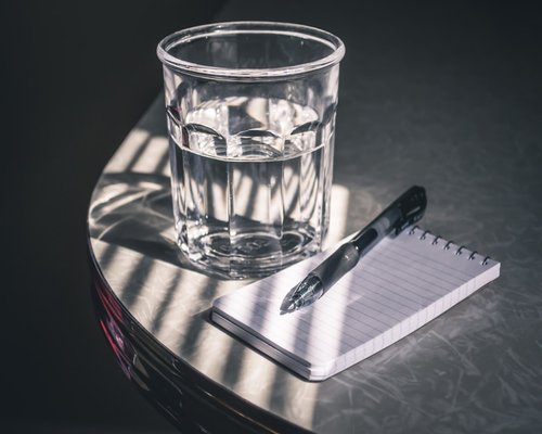A well organized desk with a cup of water and natural light